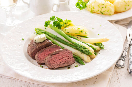Traditional roasted angus beef steak with white and green asparagus, boild potatoes and sauce hollandaise served as close-up on a classic plate