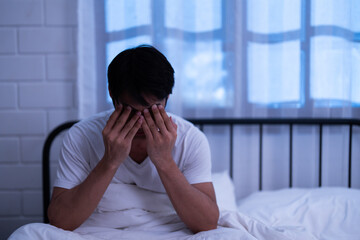 Asian insomnia man covering his face with two hands and massage eyes while sitting on the bed overwhelmed by fatigued and exhausted of disrupted sleep and rest in the bedroom night - obrazy, fototapety, plakaty
