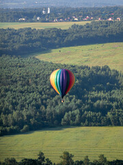 Obraz premium A colorful hot air balloon flies over the forest and fields. Early summer morning. Balloon flight.