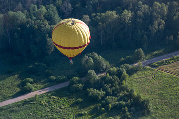 A colorful hot air balloon flies over a field and a road. Summer morning. Balloon flight.