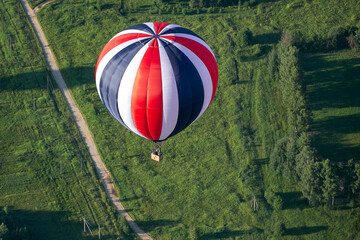 A colorful hot air balloon flies over a field and a road. Summer morning. Balloon flight.