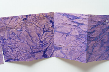 two pieces of folded paper with texture in purple