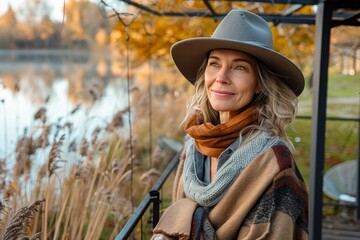 A stylish woman embraces the changing season, smiling as she dons a sun hat and scarf while surrounded by the warm hues of autumn foliage