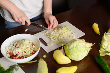 Woman prepares a vegan salad and cuts white cabbage. Close-up of a woman hands chopping white cabbage on a cutting board on the kitchen table. Veganism and raw food diet concept. 
