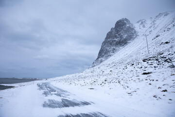 Icy road on Lofoten Islands with snow covered mountains and cloady skies