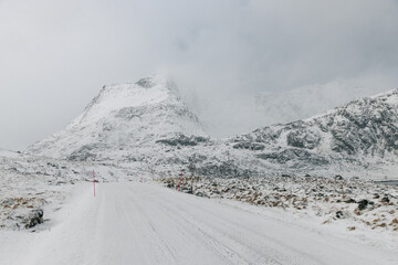 Icy road on Lofoten Islands with snow covered mountains and cloady skies