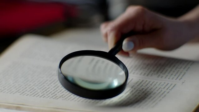 Woman reads book with magnifying glass in library	