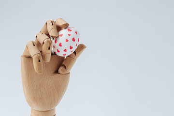 a wooden hand holding a white Easter egg with drawn red hearts stands on a white background