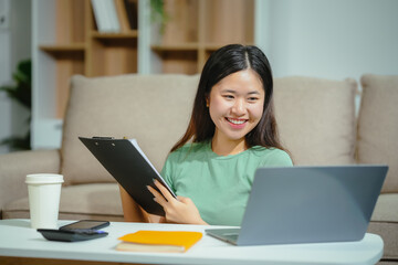 young Asian girl engages in online learning, doing homework on her sofa in the living room. video...