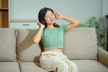 young Asian woman relaxes on the sofa, listening to music. She enjoys a moment of tranquility, immersed in the melodies that bring joy to her day.