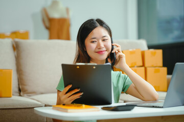 Fototapeta premium young Asian entrepreneur, the owner of a small clothing store, organizes online live streams showcasing products packaged in cardboard boxes, ensuring prompt and efficient delivery.