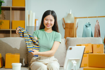 young Asian entrepreneur, the owner of a small clothing store, organizes online live streams showcasing products packaged in cardboard boxes, ensuring prompt and efficient delivery.