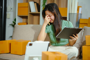 young Asian SME owner of a clothing store faces stress and sadness due to online challenges. Handling cardboard boxes and managing delivery, the struggle reflects in emotions.