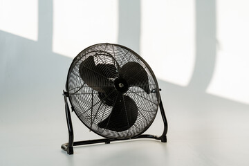 A black mechanical fan rests on a white surface near a window