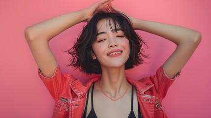Fototapeta premium Joyful Asian woman with bob haircut in red jacket against pink background.