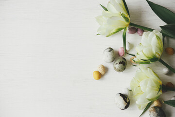 Stylish easter eggs and tulips on rustic white table. Happy Easter! Easter flat lay. Modern natural dye marble and candy chocolate eggs with spring flowers border. Space for text