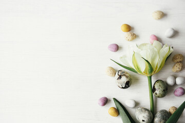 Happy Easter! Stylish easter eggs and tulip on rustic white table flat lay. Modern natural dye marble and candy chocolate eggs with spring flower. Easter festive border, space for text