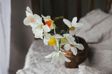 Beautiful daffodils in vintage vase on rustic wooden chair with linen cloth. Countryside floral still life. Rural moody spring flowers composition. Easter banner