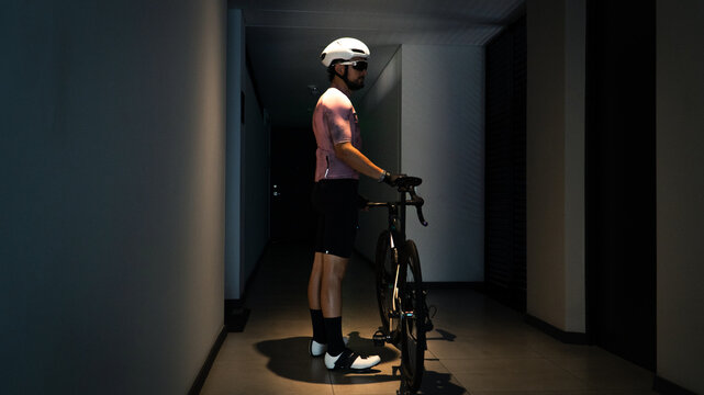 Professional cyclist waiting for the elevator in the hallway under a yellow light with his bike in his hands