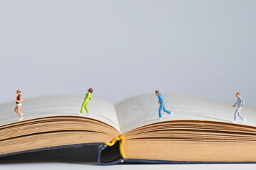 Photography of miniature people and toy figures, joggers running across an open book
​