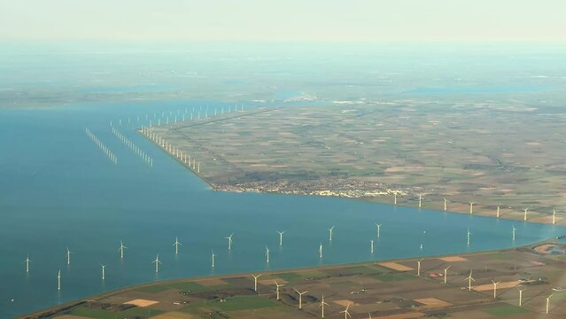Aerial film of electric renewable energy wind mills or wind turbines in IJsselmeer, a large lake in the Netherlands, Holland, with dikes and polder visible, new land with meadows and blue water