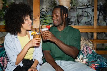 joyful young couple laughing and enjoying cocktails on a rustic café patio, evoking togetherness