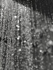 This black-and-white photograph showcases a close-up view of water in motion, with sunlight highlighting the details in individual droplets, creating a mesmerizing pattern of light and shadow. The flo