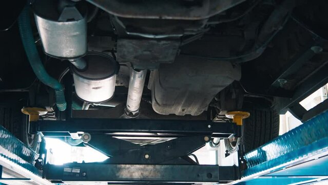 A car on a pneumatic lift at an auto repair shop, revealing its undercarriage with vehicle's exhaust system, chassis, and tires, indicative of a routine service or repair for diagnostics and
