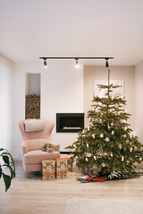 Beautiful New Year decor with a Christmas tree, an armchair and a fireplace