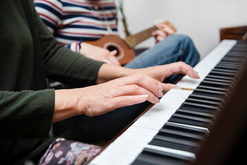 A woman plays the piano at home, her teenage daughter plays the ukulele next to her, they learn a new melody, through music, mother and daughter become closer