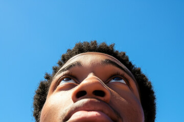Close-up of a man looking up with hope in his eyes, clear blue sky in the background, embodying optimism and aspirations