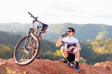 Brazilian cyclist enjoying a break atop a mountain, hydrating with water while soaking in nature's...
