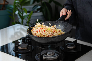 Close up of Chef cook hands cooking and toss roasted vegetables with rice for Asian cuisine in frying wok pan on gas stove. Flying food levitation.
