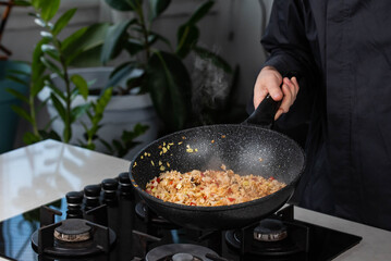 Close up of Chef cook hands cooking roasted vegetables with rice for Asian cuisine in frying wok pan on gas stove.
