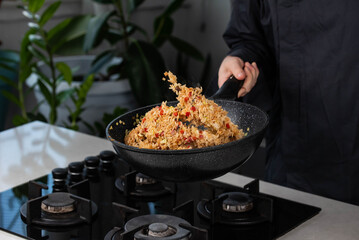 Close up of Chef cook hands cooking and toss roasted vegetables with rice for Asian cuisine in frying wok pan on gas stove. Flying food levitation.