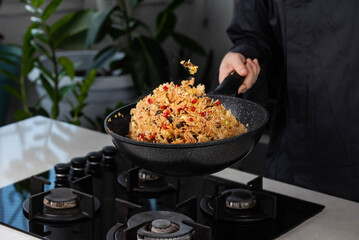 Close up of Chef cook hands cooking and toss roasted vegetables with rice for Asian cuisine in frying wok pan on gas stove. Flying food levitation.
