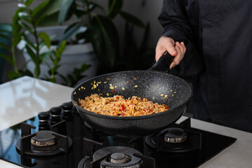 Close up of Chef cook hands cooking roasted vegetables with rice for Asian cuisine in frying wok pan on gas stove.