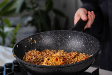Close up of Chef cook hands cooking roasted vegetables with rice for Asian cuisine in frying wok pan on gas stove.