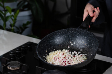 Close up of Chef cook hands cooking roasted onion and garlic in frying wok pan on gas stove.