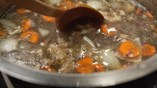 Bone broth with carrots and spices is stirred with a large wooden spoon