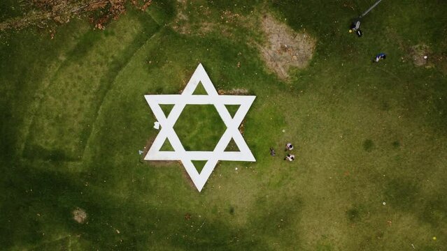 A drone flies up from the Star of David on a square in a park