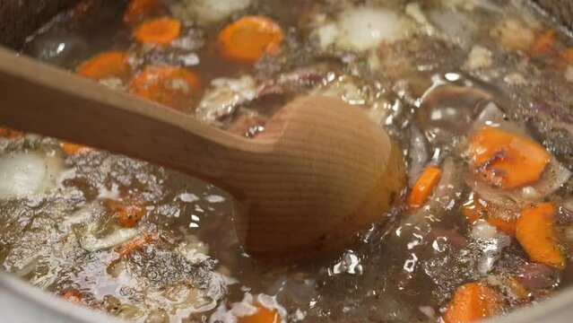Rich and fatty bone broth is stirred with a large wooden spoon