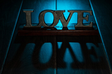 Love, a textured sign in metal, on a wooden table with backlit, cool, blue light.