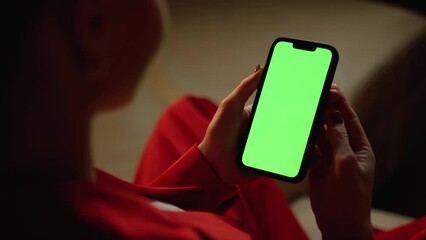 An over-the-shoulder view captures a woman using a smartphone with a green screen, potentially browsing or awaiting interaction.