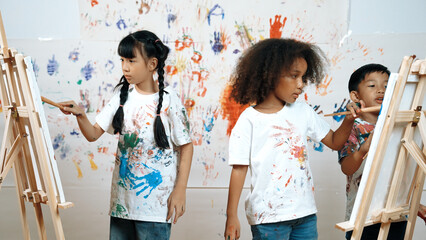 Diverse student painted or draw canvas at stained wall in art lesson. Asian girl wearing white...