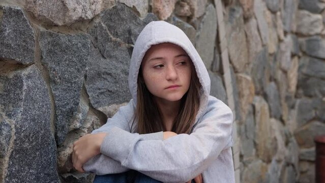 Sad depressed teenage girl in a hood sleeps alone on the street, feeling angry and lonely. Growing crisis and anxiety. Concept of self-acceptance and self-analysis. Homeless