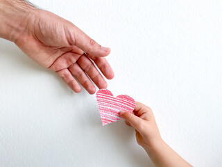 Adult hand giving striped pink paper heart to childs hand, concept of love, care, and family bonding with copy space. Can be utilized for materials about parenting, child development, and family