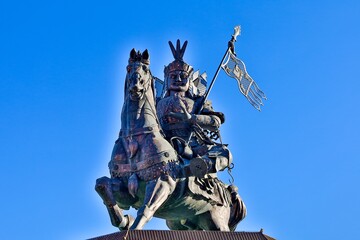 A majestic bronze statue of King Gesar, the legendary hero of Tibetan folklore, stands tall against the backdrop of a serene blue sky in Gyegu Town, Yushu, Tibet.