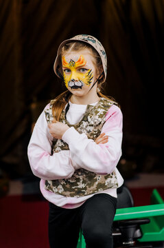 Girl, child stands in military camouflage, khaki uniform, face painted with strong tiger makeup. Photography, Ukrainian pariot.