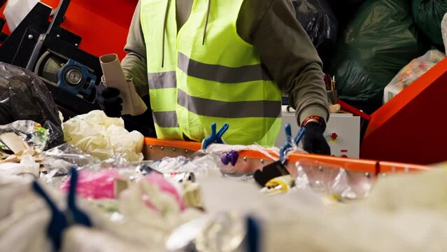 close-up of a sorting line in the background a worker in a protective suit while working at a waste processing plant